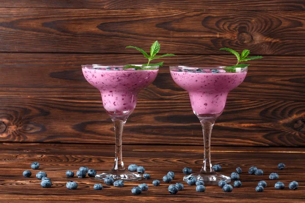 İki bardak taze yüzlü ile. Lezzetli smoothies ahşap arka plan üzerinde. Yaban mersini, nane ve ahududu ile doğal içecekler.