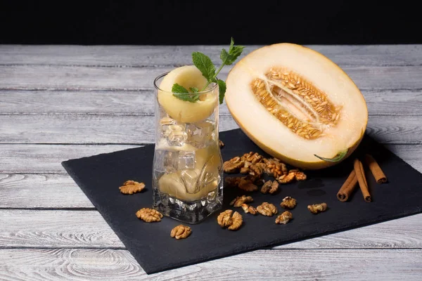A fresh sweet melon, walnuts and a glass of ice, mint and honeydew on a wooden background. Natural ingredients. A cut cantaloupe.