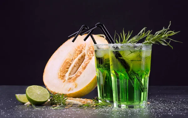 Bebidas refrescantes sin alcohol. Corte el melón y los cócteles verdes sobre un fondo negro. Bebidas dulces con licor, lima y estragón . — Foto de Stock