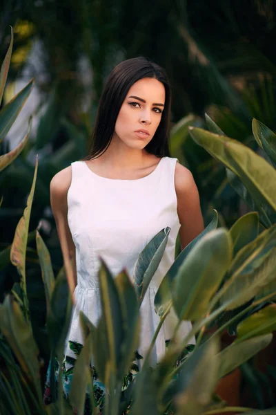 Een aantrekkelijke brunette meisje. Een doordachte jonge vrouw. Een dame in een witte jurk op een tropische tuin achtergrond. Een sensuele meisje. — Stockfoto