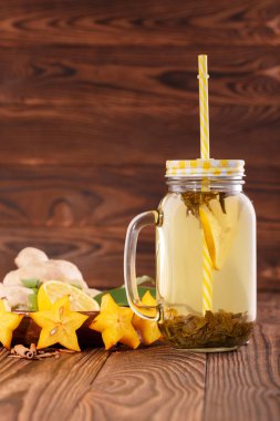 Vitamini içecek bardağı taşıran damla limon, zencefil ve ahşap arka plan üzerinde carambola yanında büyük bir kavanoza close-up. Kopya alanı.