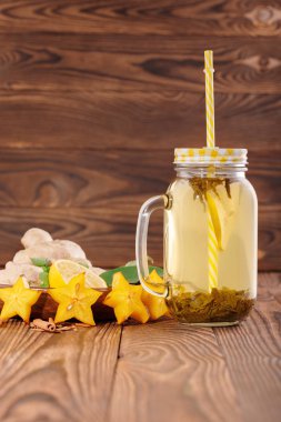 Büyük kavanoz bir close-up ile kesilmiş limon, nane, zencefil ve ahşap arka plan üzerinde carambola yanında bitkisel çay saman dolu. Kopya alanı.