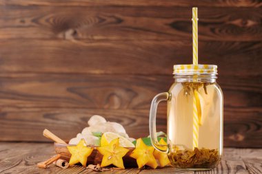 Sarı meşrubat bardağı taşıran damla kesilmiş limon, tarçın, zencefil ve ahşap arka plan üzerinde carambola yanında büyük bir mason kavanoza. Kopya alanı.