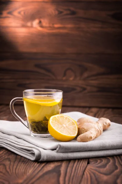 Té ecológico verde. Una taza de té sobre un fondo de madera oscura. Una taza de vidrio llena de líquido, hojas de té verde natural y limón . — Foto de Stock