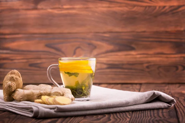 Una taza de bebida de menta amarilla. Una taza de té en una mesa de madera oscura. Una hermosa taza con limón cortado y jengibre orgánico. Copiar espacio . — Foto de Stock
