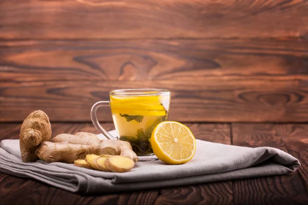 Una taza llena de té verde. Una taza sobre un fondo de madera. Una taza pequeña junto a jengibre y limón en un mantel. Copiar espacio . — Foto de Stock