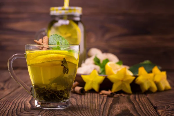 Una pequeña taza llena de té verde limón sobre un fondo de madera oscura. Una taza de té dulce junto a carambola, jengibre y menta. Copiar espacio . — Foto de Stock