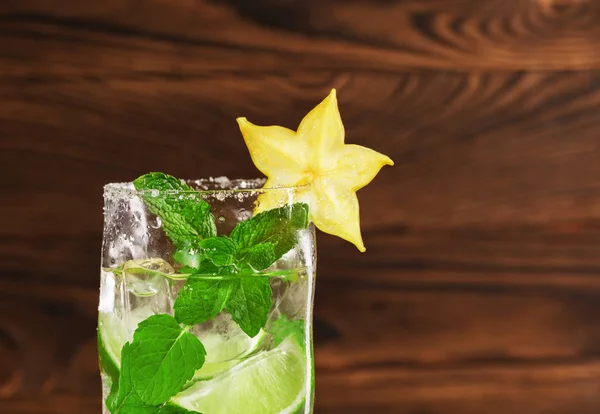 Nahaufnahme eines alkoholischen Mojito-Getränks mit frischer Limette, Minze, Eis und dekorativem Karambolage auf dunklem Holzgrund. Kopierraum. — Stockfoto