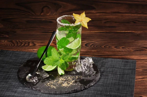 A green mojito with a spoon. A mojito cocktail on a wooden background. Mint, ice and carambola on an alcoholic drink. Copy space.