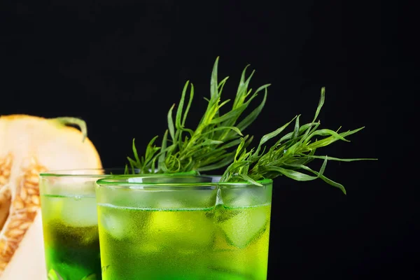 Nahaufnahme eines Estragon-Getränks. ein Glas grünen alkoholischen Limettencocktail. kaltes Kräutergetränk und süße Melone auf schwarzem Hintergrund. — Stockfoto