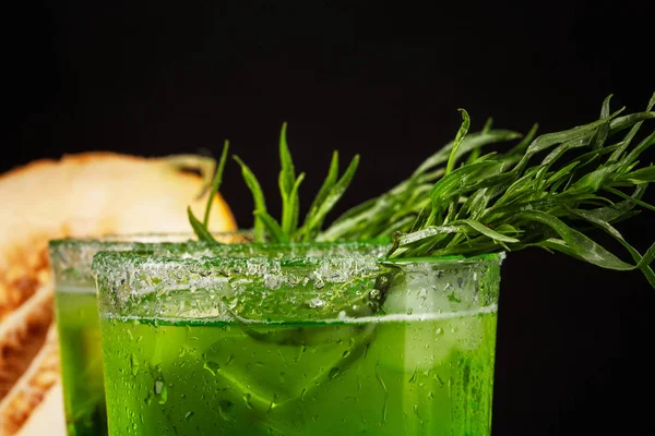 Nahaufnahme eines Estragon-Getränks. ein Glas grünen alkoholischen Limettencocktail. kaltes Kräutergetränk und süße Melone auf schwarzem Hintergrund. — Stockfoto