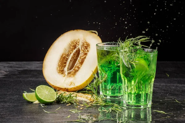 İki parlak tarhun sıçramasına kokteyller siyah bir zemin üzerine close-up. Tarhun ile içecekler, tatlı kavun, buz küpleri ve Ekşi limon kesmek.