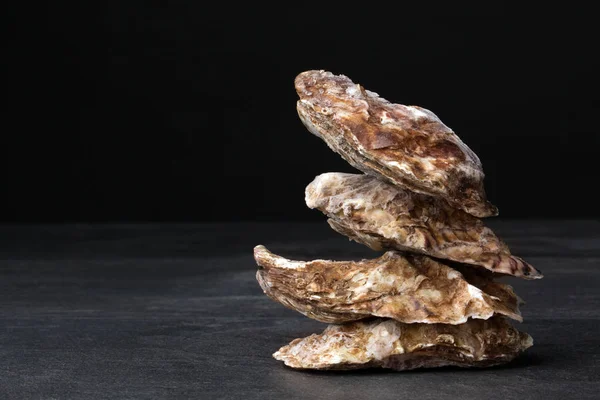 A group of freshly and raw shucked oysters on a black background. Chilled raw oysters. Delicious tropical sea mollusk. — Stock Photo, Image