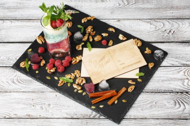 Güzel bir kompozisyon güzel kartpostallar ve ışık gri arka plan üzerinde renkli kokteyl. Birçok çilek, ceviz, tarçın ve yeşil yaprakları davetiye.