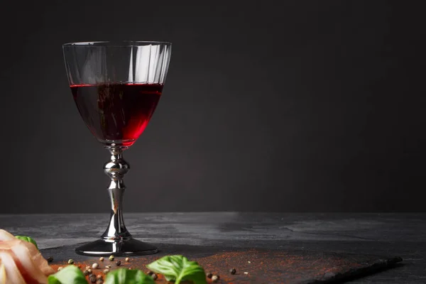 Бокал темно-красного вина и куча разрезанного мяса на черном фоне. Прошутто, ароматно-зеленый базилик и перец на столе. Копирование пространства . — стоковое фото
