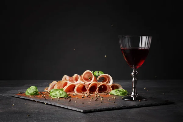 Eine schöne Komposition aus appetitanregendem Prosciutto, Rotwein und Basilikum auf schwarzem Hintergrund. Feinkost, Luxus, Festkonzept. Kopierraum. — Stockfoto