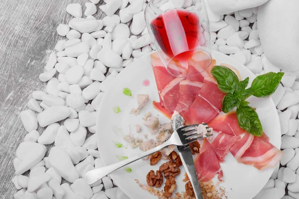 Los restos de alimentos caros en un plato de cerámica con un cuchillo y tenedor sobre un fondo de piedras blancas. Una copa de vino tinto seco cerca del plato. Copiar espacio . — Foto de Stock