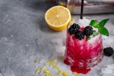 Viski bardak berry pembe kokteyl ve metal bir shaker close-up. İçecek nane, limon ve böğürtlen gri bir arka plan üzerinde. Kopya alanı.