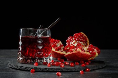 Alkollü kokteyl serinletici. Bir bardak kırmızı içecek ve siyah bir arka plan üzerinde olgunlaşmış bir Granat bileşimi. Kırmızı meyveli içecek.