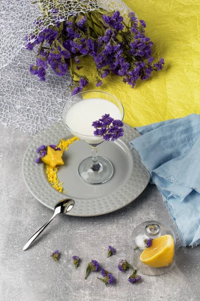 Μια κορυφαία θέα από ψηλά ένα ποτήρι μαργαρίτα γεμίζουν με γάλα φρέσκο, γλυκό και βιολογικό αναψυκτικό σε ένα πολύχρωμο φόντο. Τα λεμόνια ζουμερά, ώριμα και όμορφα λουλούδια σε ένα ύφασμα. — Φωτογραφία Αρχείου