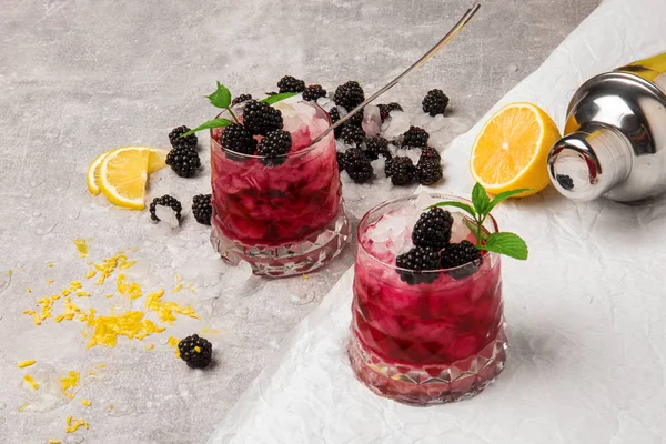 Blick von oben auf zwei große Gläser kalte Getränke mit Beeren und Eis auf grau-weißem Hintergrund. gesunde und biologische Brombeeren, Zitrone und Minze. — Stockfoto