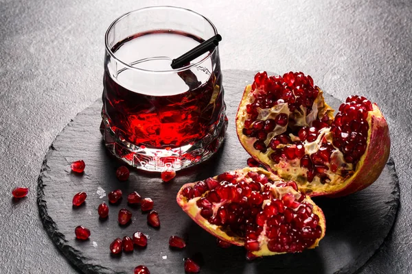 Ljusa garnet drink och ett rött granatäpple på en grå bakgrund. Exotiska ingredienser för sommardrinkar. Friska delikatess. — Stockfoto
