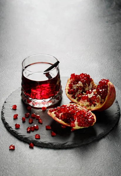 Bright garnet drink and a tropical pomegranate on a light gray background. Exotic ingredients for summer cocktails. Copy space. — Stock Photo, Image