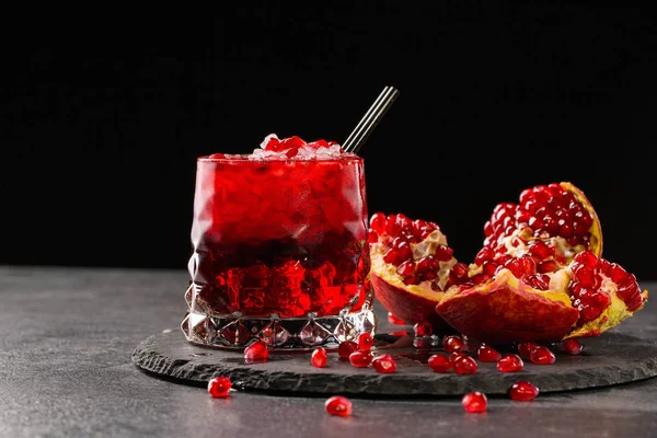 Una copa de cóctel de bayas. Semillas de granate rojo. Bebida fresca con hielo y una granada madura sobre un fondo negro. Bebidas caras . — Foto de Stock