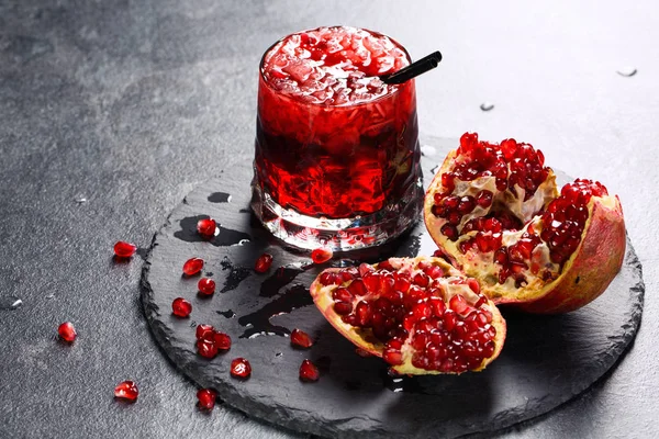 En uppfriskande exotiska dryck och ett snitt garnet på en grå bakgrund. Rött alkoholfritt juice med is. Kalla bitterljuv drycker. — Stockfoto