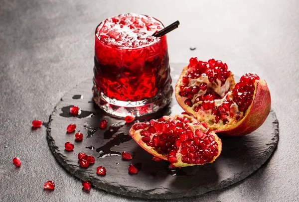 Una refrescante bebida afrutada y un granate cortado sobre un fondo gris. Bebida roja sin alcohol con hielo. Bebidas frescas agridulces . — Foto de Stock