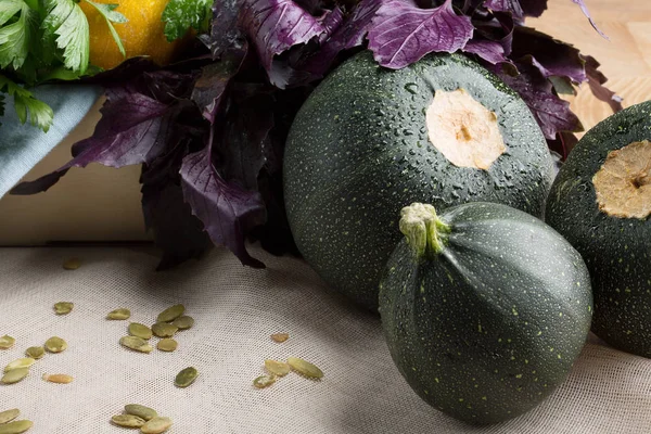 A group of three round green and yellow zucchinis on a wooden background. A bunch of fresh, raw parsley and basil.