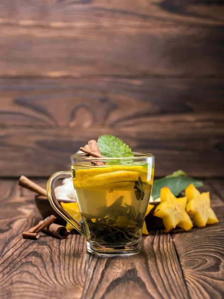 Una taza de té de limón con menta sobre un fondo borroso de madera. Té caliente con carambola y palitos de canela. Copiar espacio . — Foto de Stock