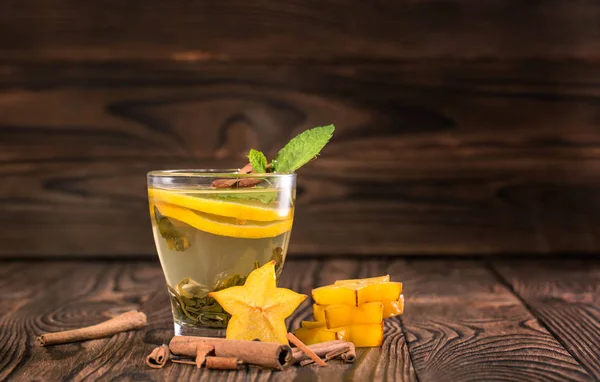 Una taza de té de limón con menta verde sobre un fondo borroso de madera. Té caliente con carambola y palitos de canela . — Foto de Stock