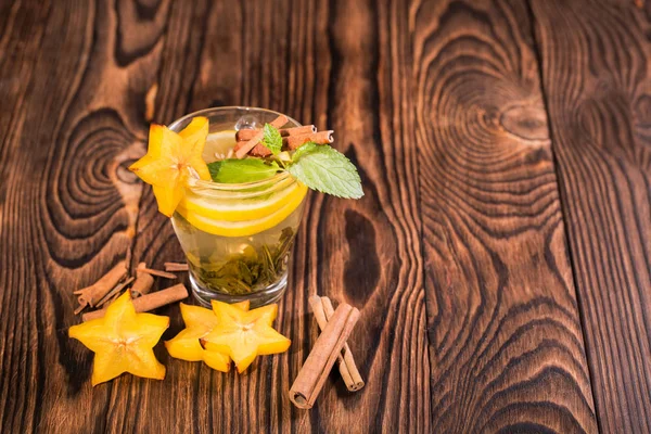 Una taza de té de limón con menta verde sobre un fondo borroso de madera. Té caliente con carambola y palitos de canela . — Foto de Stock