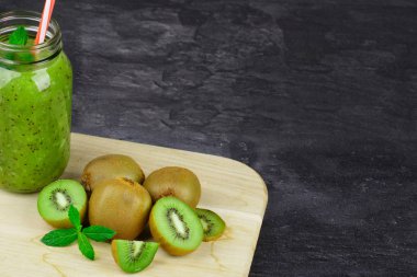 Kivi içecek ile dolu bir mason kavanoza karanlık bir taş zemin üzerine bir ışık ahşap tahta üzerinde nane yaprakları. Kopya alanı.