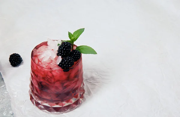 Cocktail di ghiaccio con menta fresca e more in un bicchiere rosa su sfondo bianco, tovaglia liscia bianca. Bevande estive . — Foto Stock