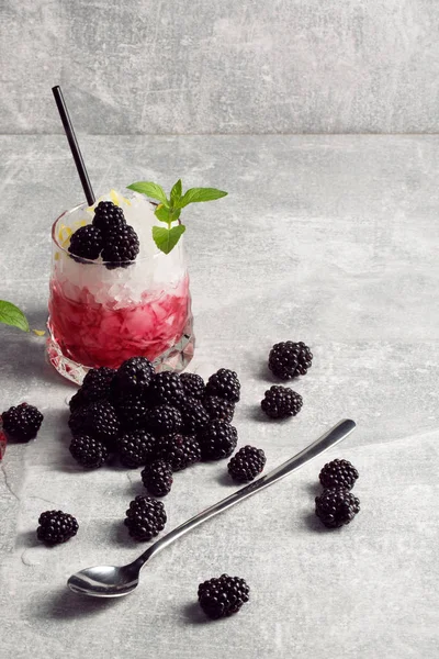 Bir bardak meyve kokteyl ve buz, çilek ve nane, gümüş çay kaşığı yaprak gri bir arka plan üzerinde bir tablo ile.