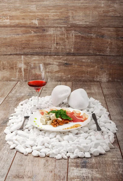 Ein Teller mit Prosciutto, Roquefort, Walnüssen und Basilikum, ein Glas Rotwein auf weißem Stein. — Stockfoto