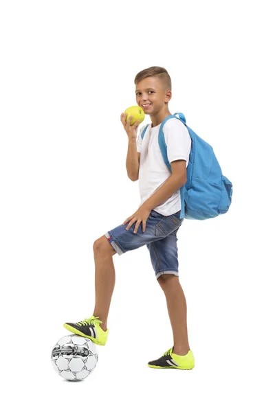 Школярка їсть яблуко ізольовано на білому тлі. Учень пробиває футбольний м'яч. Концепція шкільного футболу та футболу . — стокове фото