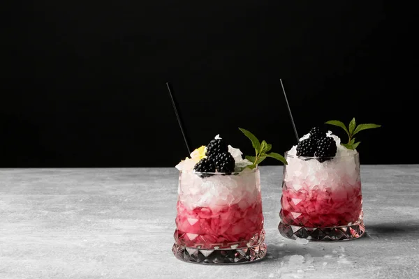 Zwei Gläser mit Saft und Eis, Trinkhalme, grüne Minzblätter auf grauem Tisch vor schwarzem Hintergrund. — Stockfoto