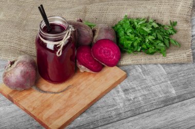 İçecek bardağı taşıran damla kumaş ve ahşap arka plan ile bir mason kavanoz. Kırmızı beetroots ve maydanoz bir kesme tahtası üzerinde.
