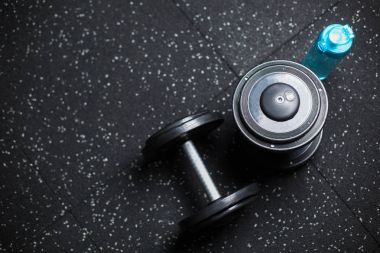 İki metal dumbell ve bir şişe su, bulanık bir arka plan üzerinde ağırlık spor rutin için donatım için Üstten Görünüm.