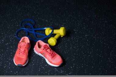 Koyu kırmızı parlak spor ayakkabı, sarı canlı dambıl, mavi genişletici, karanlık bir arka plan bulanık bir egzersiz için donatım.