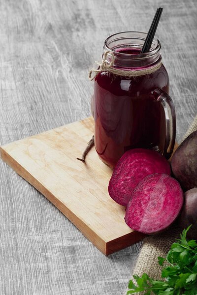 A mason jar of beetroot juice full of vitamins on a wooden background. Slices of beets and parsley on a cutting board.