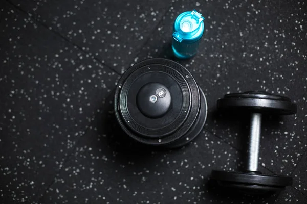 Top view of metal dumbbells and a blue bottle for water, stuff for sports routines on a dark blurred background.