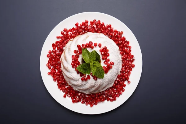 Einen Teller mit Obstkuchen. Kuchen bedeckt mit Pulver und saftigen Granatkernen. ein Ringkuchen mit aromatischer Minze. Bäckereikonzept. — Stockfoto