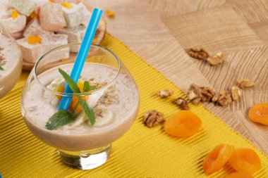 Bir bardak rendelenmiş ceviz, muz dilimleri ve nane yaprakları, lokum bulanık renkli arka plan üzerinde bir tabak.