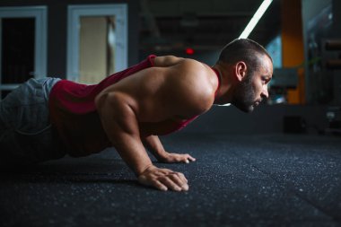 Spor salonunda push-up yapıyor genç yakışıklı adam yan görünüm. Yakışıklı kaslı bir vücut üzerinde arka plan bulanık ile.