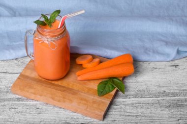 Mavi kumaş arka plan üzerinde sağlıklı havuç güler yüzlü. Kesme havuç yanındaki bir mason kavanoza sağlıklı Detoks içecek.