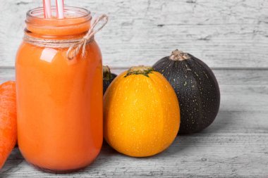 Bir mason kavanoza sağlıklı havuç suyu, sarı ve yeşil kabakları, üzerinde bir ışık ahşap arka plan bulanık soyulmuş havuç.